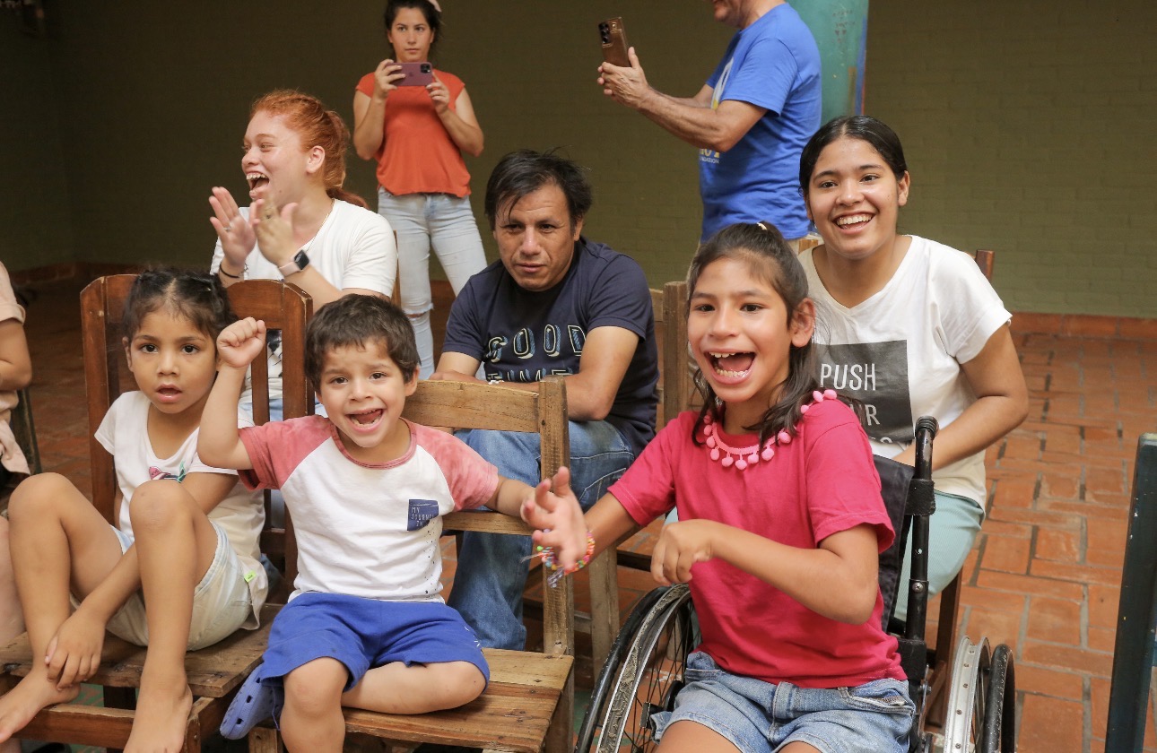 Children laughing together, including a young girl in a wheelchair